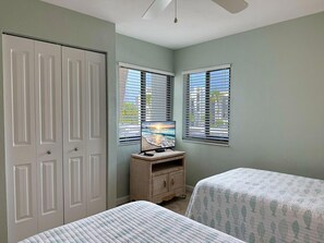 Un dormitorio con dos camas, un televisor sobre un mueble bajo, un armario y ventanas con persianas.