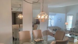 A modern living room with a glass dining table, beige chairs, and a chandelier. - Open Deck – 2BR Loft Condo with Bay Views (Englewood)