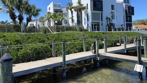 A modern building with a white facade, a wooden dock, and palm trees. - Open Deck – 2BR Loft Condo with Bay Views (Englewood)
