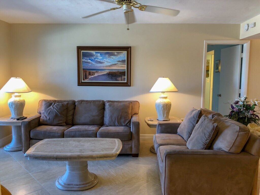 Ein Wohnzimmer mit zwei Sofas, einem Couchtisch und zwei Lampen. Eine Deckenventilator und ein gerahmtes Bild sind an der Wand zu sehen.
