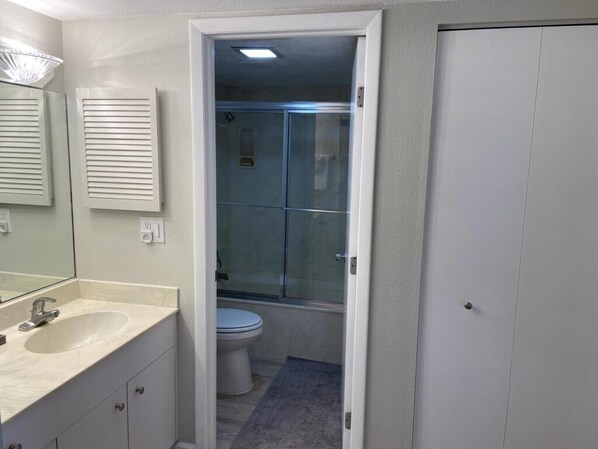 A bathroom with a sink, mirror, and toilet. There is a glass shower door and a towel rack.