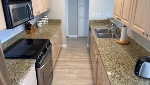 A kitchen with granite countertops, a stove, a microwave, a sink, and wooden cabinets.