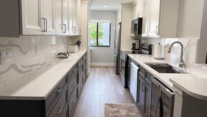 A modern kitchen with white cabinets, stainless steel appliances, and a marble countertop. - Effortless Escape – Walk-Out 2BR at Tamarind (Englewood)