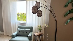 Un salon avec un fauteuil bleu clair, un pouf assorti, une petite table d’appoint ronde sur laquelle est posée une plante, et un lampadaire.