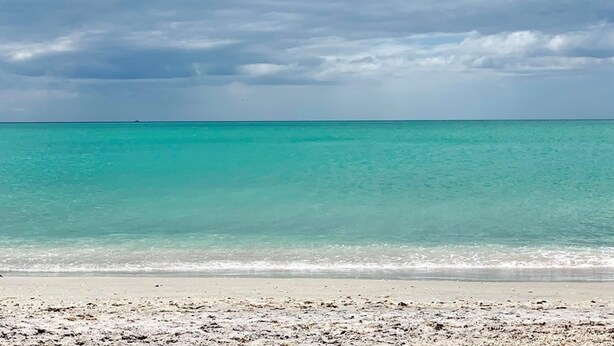 A beach with clear turquoise water and a cloudy sky.