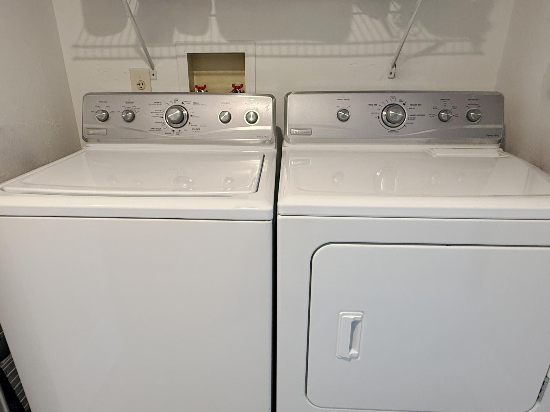 A pair of white front-loading washers with control panels, a small wooden box, and a power outlet on the wall.