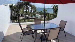 Ein Balkon mit Glastisch und Stühlen, einem roten Sonnenschirm und Blick auf einen Pool sowie Palmen.