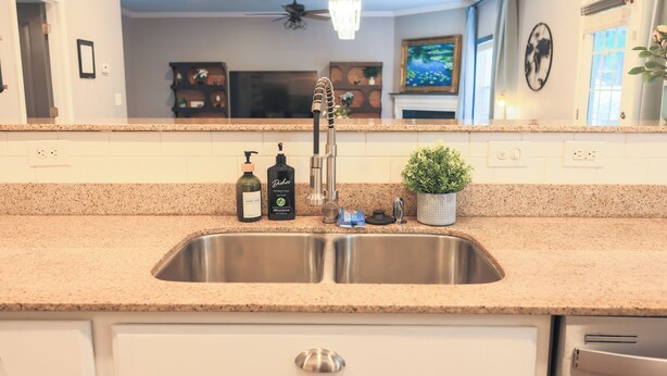 A kitchen with a stainless steel sink, granite countertop, and a ceiling fan.