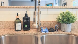 A kitchen counter with a stainless steel sink, a hand soap bottle, a dish soap bottle, a dish soap dispenser, a potted plant, and a faucet.