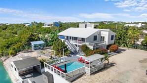 A beachfront property with a swimming pool, red lounge chairs, and a covered deck area. - Waterfront 5BR Home w/ Pool, Gated Parking & Prime Location! (Cooper Jack Bay Settlement)