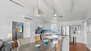 A modern kitchen with white cabinets, a central island, and a dining area with a glass table and patterned chairs. - Waterfront 5BR Home w/ Pool, Gated Parking & Prime Location! (Cooper Jack Bay Settlement)