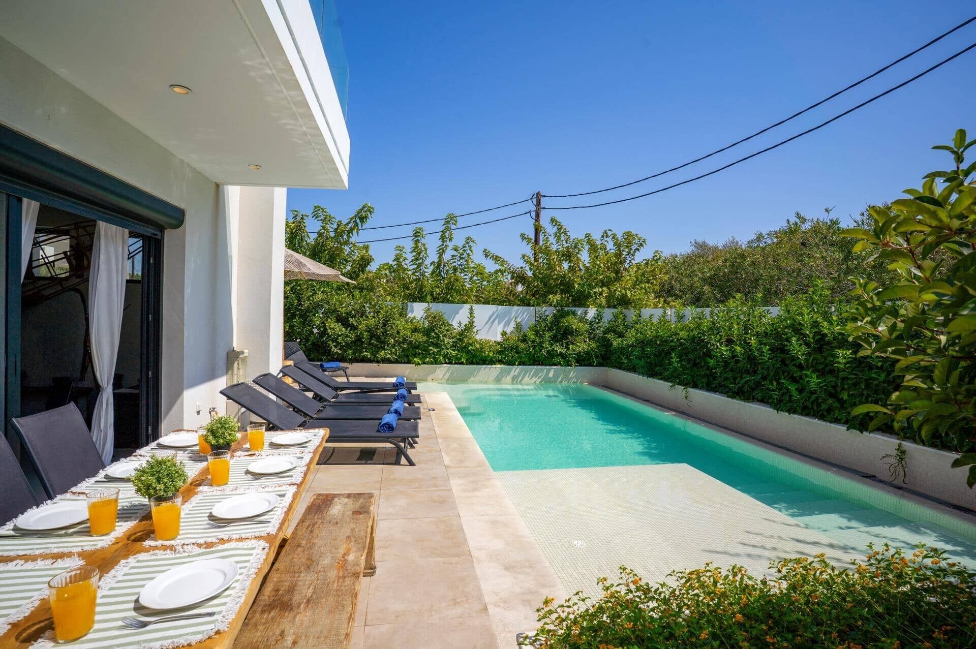A poolside area with a dining table set for four, surrounded by lounge chairs, and a clear blue pool.