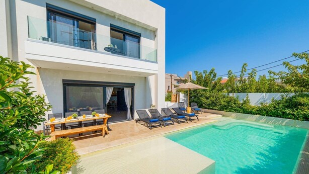 Une maison moderne à deux étages dotée d’une piscine, d’un espace extérieur aménagé et d’une végétation luxuriante.