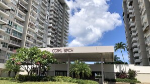 Un edificio residencial de varios pisos con balcones, un letrero que dice "CORAL BEACH" y abundante vegetación circundante.