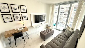 Un salon moderne avec un canapé, une table basse, un téléviseur et des œuvres d’art encadrées accrochées au mur.