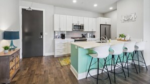 A modern kitchen with white cabinets, a central island with bar stools, a microwave, and a refrigerator. - 2BR/2BA Luxury Bywater Condo In New Orleans! (New Orleans)