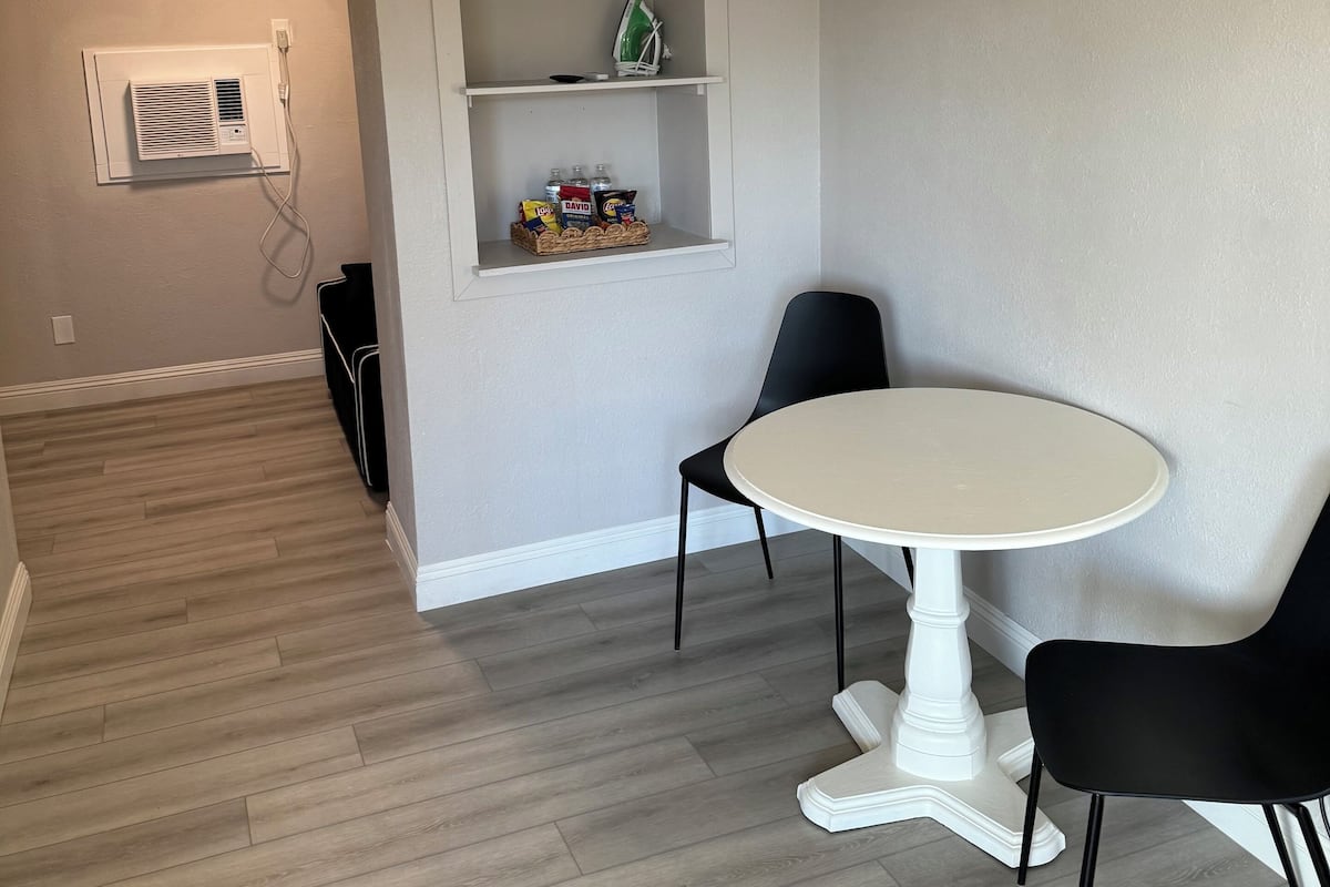 A room with a white round table, black chairs, a white air conditioning unit, and a shelf with cleaning supplies.