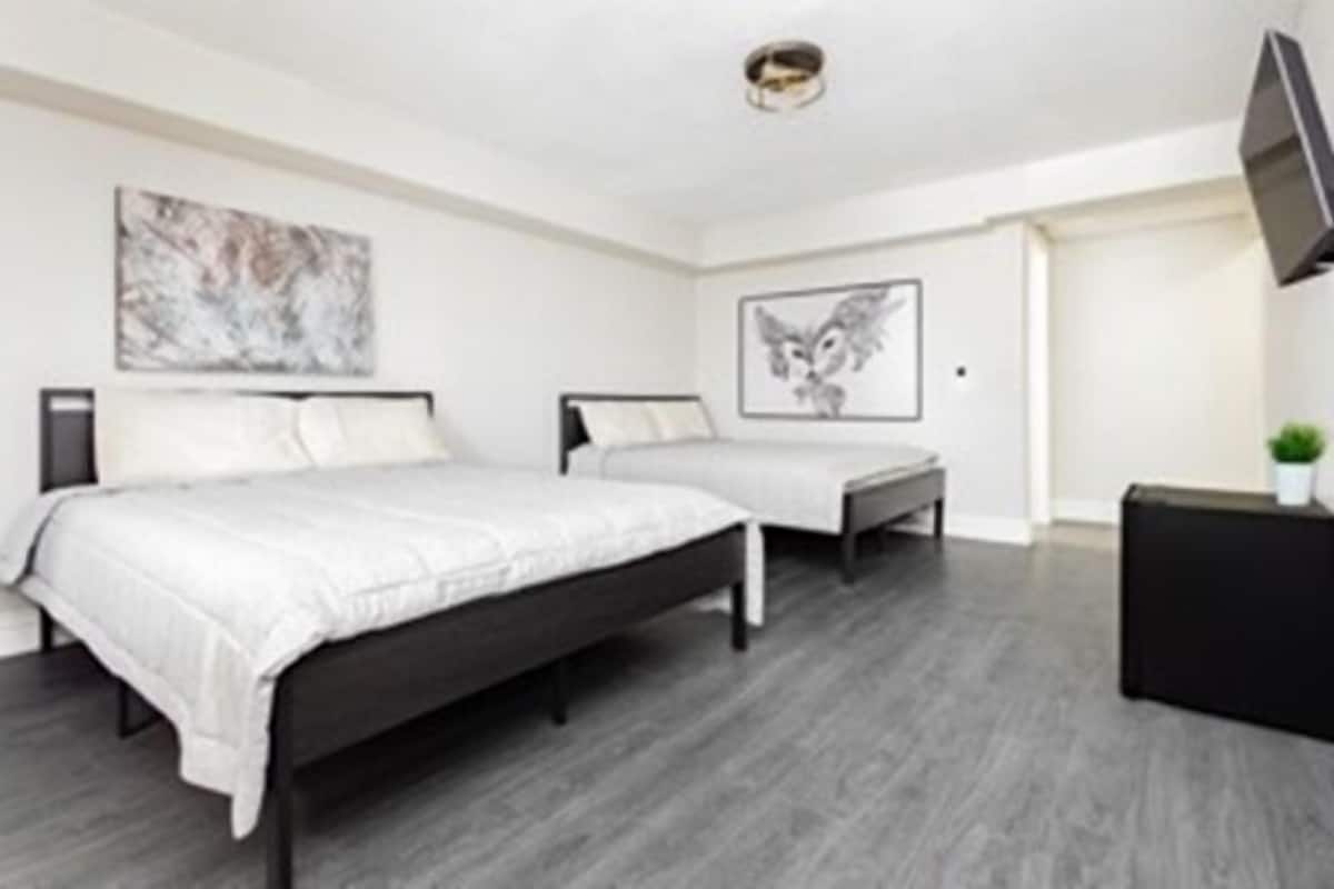 A modern bedroom with two beds, a flat-screen TV, and artwork on the walls.