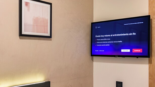 Een televisie aan een muur bevestigd, waarop een Netflix-interface wordt getoond met een bericht over exclusieve content en abonnementen.
