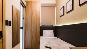 Een kleine hotelkamer met een bed, nachtkastje, kledingkast en een bureau.