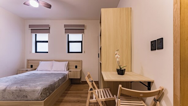Une chambre à coucher avec un lit, un bureau, une chaise et une petite table sur laquelle est posée une plante.