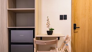 Une pièce de taille modeste, avec un bureau en bois, une petite chaise, une orchidée en pot et un réfrigérateur Hisense.