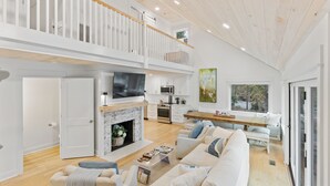 A spacious living room with a fireplace, a large TV, and a dining area with a wooden table and benches. - Lake Norman Lake Access, Hot Tub & Dock (Mooresville)