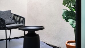 Un área de estar exterior moderna con una silla y una mesa negras, una planta en maceta y una pared con textura.