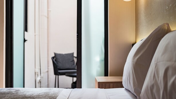 Una habitación de hotel con una cama, una mesita de noche y una silla al fondo.