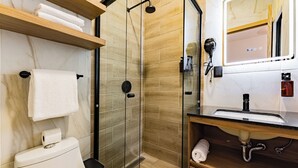 Un baño moderno con ducha envuelta en vidrio, tocador de madera con lavamanos y espejo sobre el tocador.