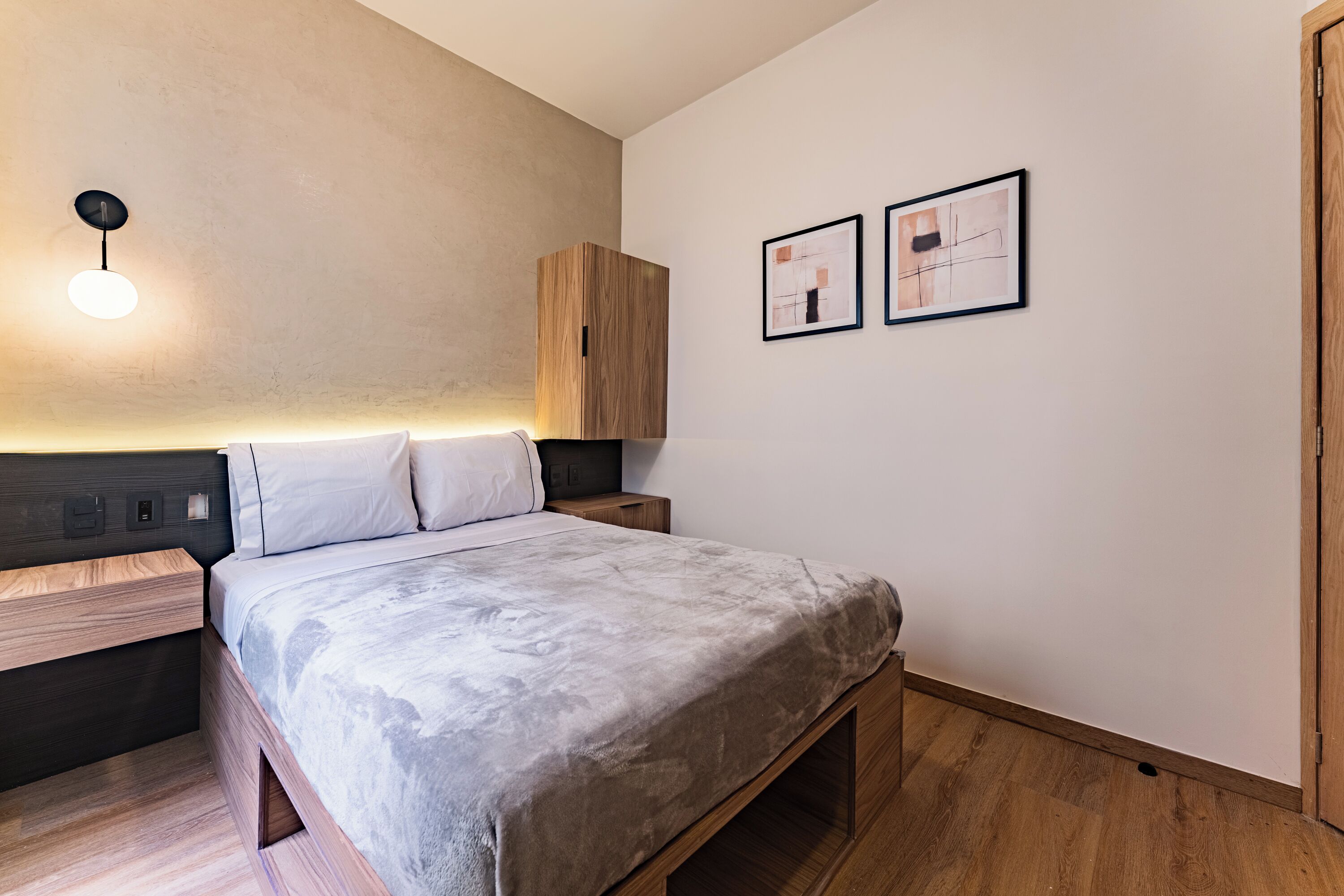 A modern bedroom with a bed, wooden headboard, bedside tables, and a wall-mounted light fixture.