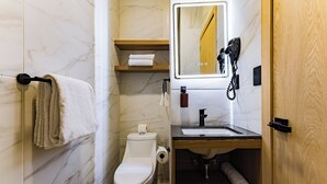 A modern bathroom with a toilet, sink, and mirror. There are towels on a rack, a hairdryer, and a bottle on the counter. - Private suites in remodeled old house in Roma Norte (Mexico)
