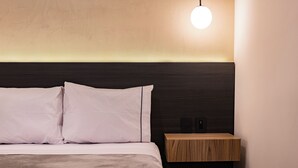 A neatly made bed with white linens and two pillows, a wooden bedside table with a light fixture above, and a dark headboard. - Private suites in remodeled old house in Roma Norte (Mexico)