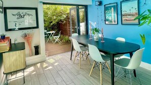 A modern dining area with a dark table, white chairs, and a glass door leading to an outdoor patio. - Townhouse by Notting Hill - Sleeps5/petsok/tv/wifi (London)