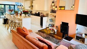 A modern living room with a sofa, coffee table, and a TV. There is a kitchen area with white cabinets and a dining area with chairs. - Townhouse by Notting Hill - Sleeps5/petsok/tv/wifi (London)