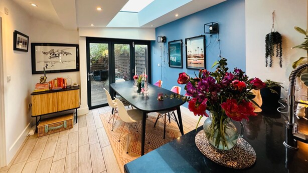A modern dining area with a skylight, a black dining table, and chairs. There are framed pictures on the walls, a wooden cabinet, and a potted plant. - Townhouse by Notting Hill - Sleeps5/petsok/tv/wifi (London)