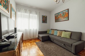 A living room with a grey sofa, a flat-screen TV, wooden flooring, and a large window with sheer curtains. - Downtown Aquarelle by Vacationy (Porto)