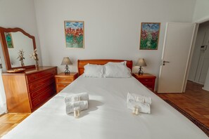 A neatly made double bed with white linens, two bedside tables with lamps, a wooden dresser, and two floral paintings on the wall. - Downtown Aquarelle by Vacationy (Porto)