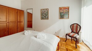 Ein Schlafzimmer mit einem großen Bett, einem Holzschrank, zwei gerahmten floralen Bildern, einem Sessel und einer Heizung.