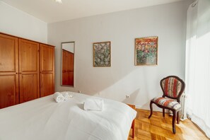 A bedroom with a large bed, wooden wardrobe, two framed floral paintings, a chair, and a radiator.