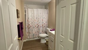 A narrow hallway leading to a bathroom with a toilet, shower curtain, and cabinets. - House centrally  (Fort Myers)