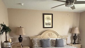 A neatly arranged bedroom with a bed, a ceiling fan, a framed picture on the wall, and a nightstand with a lamp. - House centrally  (Fort Myers)