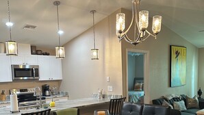 A modern kitchen with white cabinets, a stainless steel microwave, and a coffee maker. There is a dining table with chairs and a chandelier above it. - House centrally  (Fort Myers)