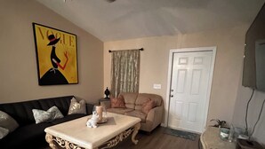 A living room with a beige sofa, a coffee table, a ceiling fan, a door, and a wall-mounted artwork. - House centrally  (Fort Myers)