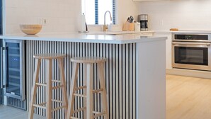 Una cucina moderna con isola centrale, sgabelli da bar, illuminazione a sospensione, una sveglia e una macchina per il caffè.