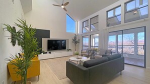 Un soggiorno spazioso con un'ampia televisione a schermo piatto, una ventola a soffitto e vista su un paesaggio desertico attraverso ampie finestre.