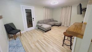 A living room with a sectional sofa, a small table, a chair, and a door with a frosted glass panel.