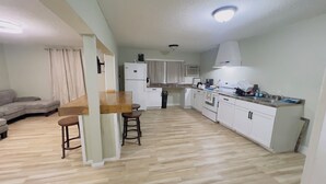 A modern kitchen with white cabinets, a wooden countertop, and a built-in oven. There is a dining area with a wooden table and two stools.