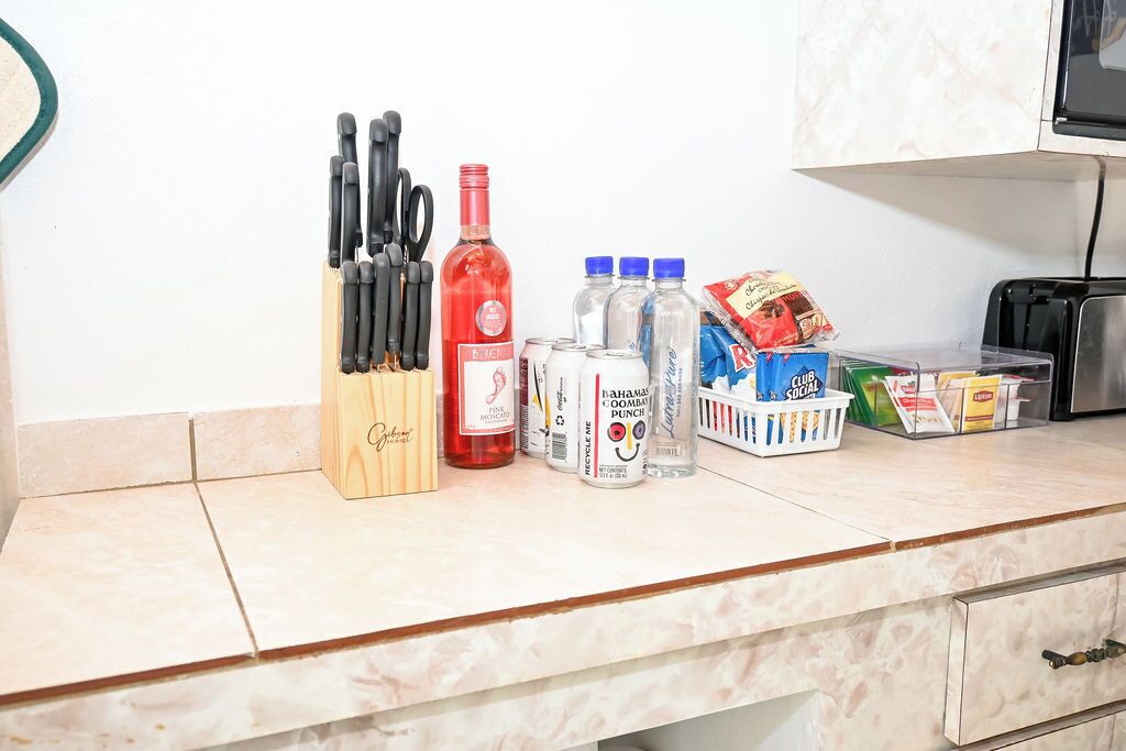 Un piano di lavoro in cucina con diversi oggetti, tra cui un portachiodi, una bottiglia di liquido rosso, bevande in lattina e un cesto di snack.