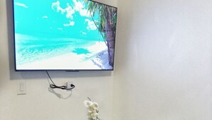 A small dining area with two chairs, a table, and a TV mounted on the wall displaying a beach scene. - Centrally Located Apartment – Dine, Explore, Relax (Rock Sound)